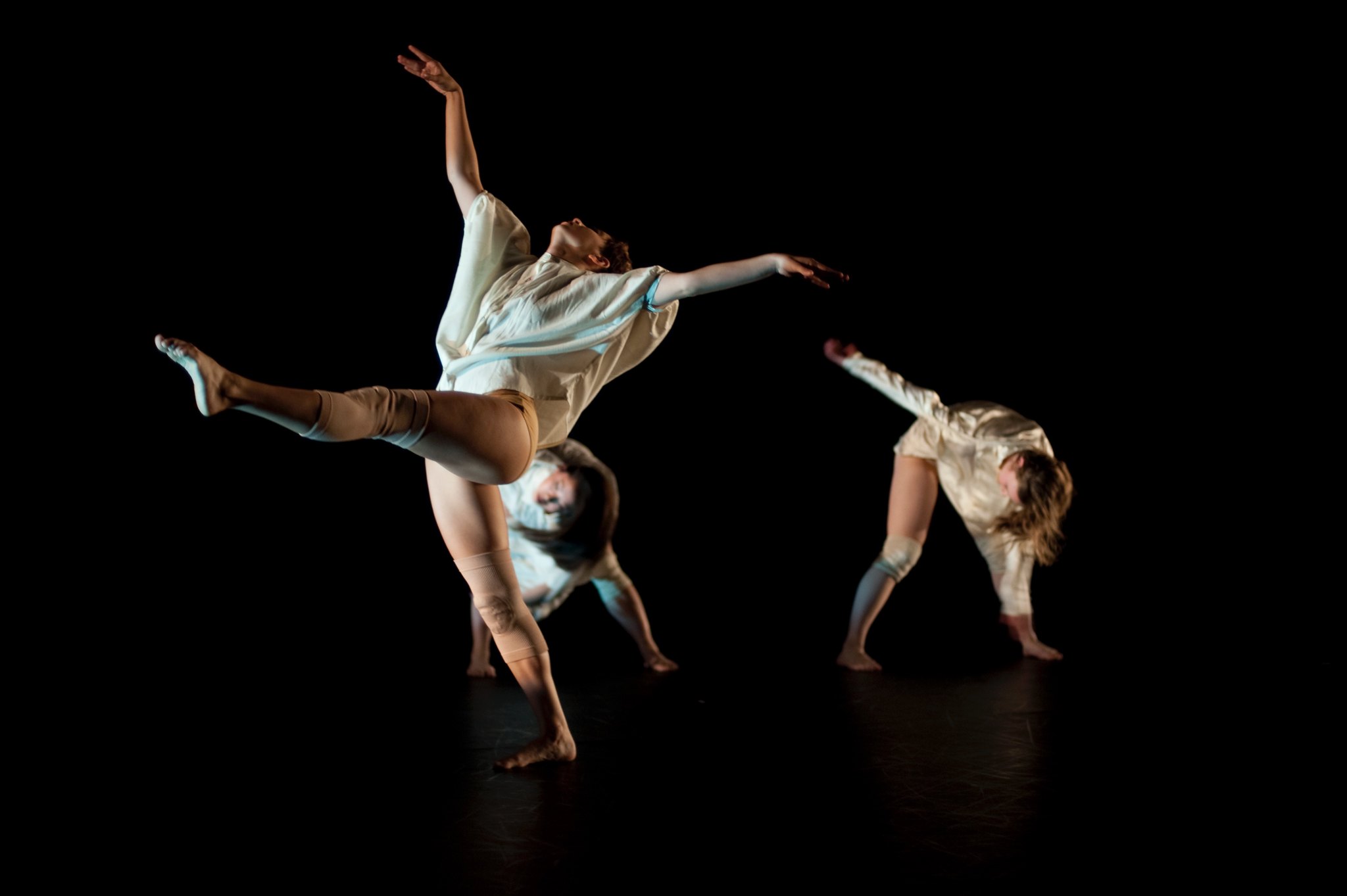 Three performers dance on stage against a dark background