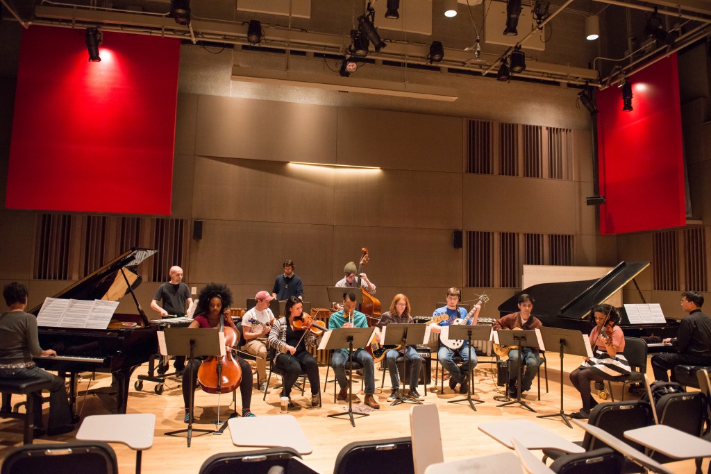 A group of musicians perform in a large room with red panels