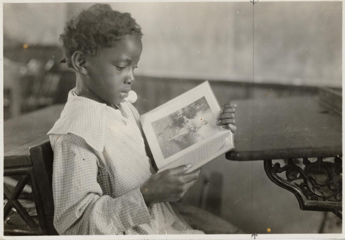 A little girl reads a book in a 1921 Lewis Hine photo