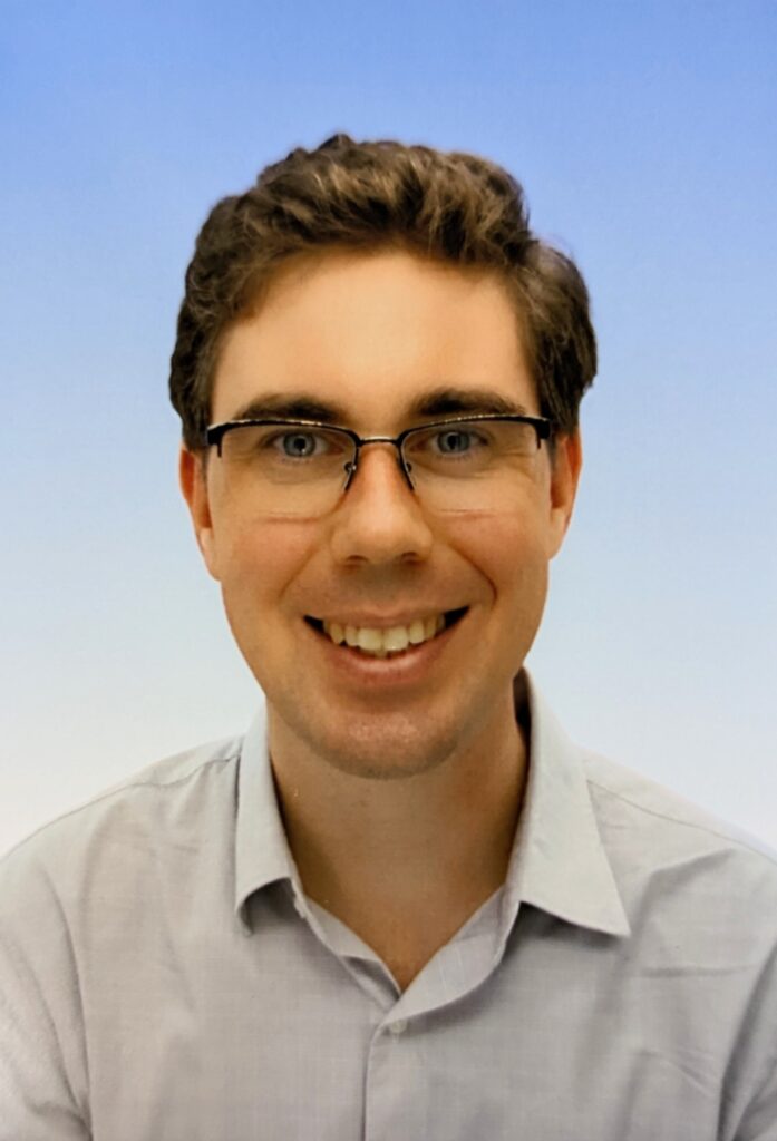 headshot of a smiling man wearing glasses and a collared dress shirt