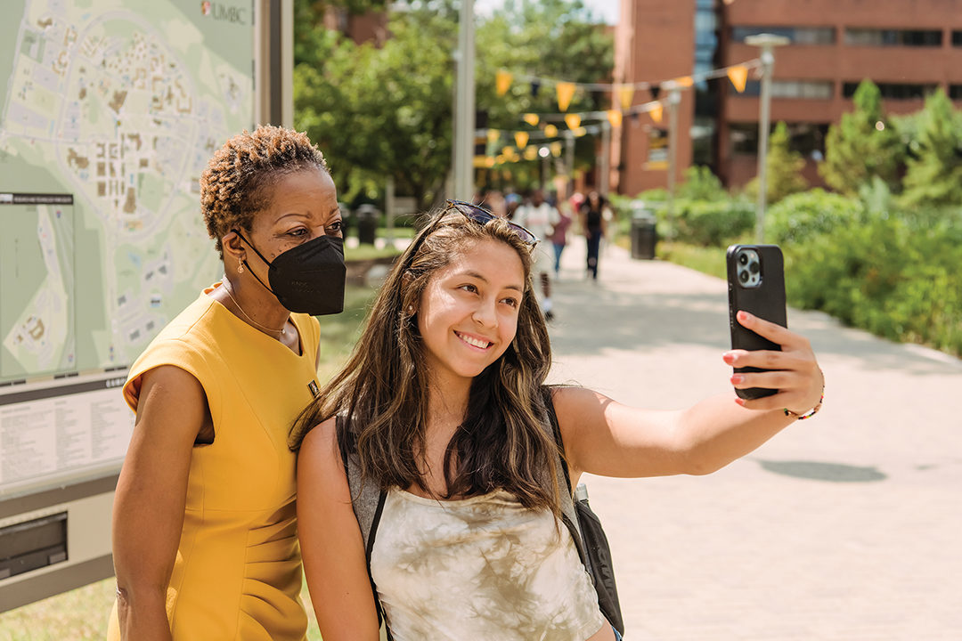 President of UMBC and a student pose on a campus walkway for a selfie.