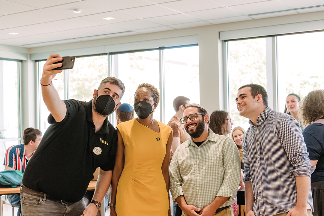 Three men pose for a selfie with the president of UMBC, who is in a gold dress.