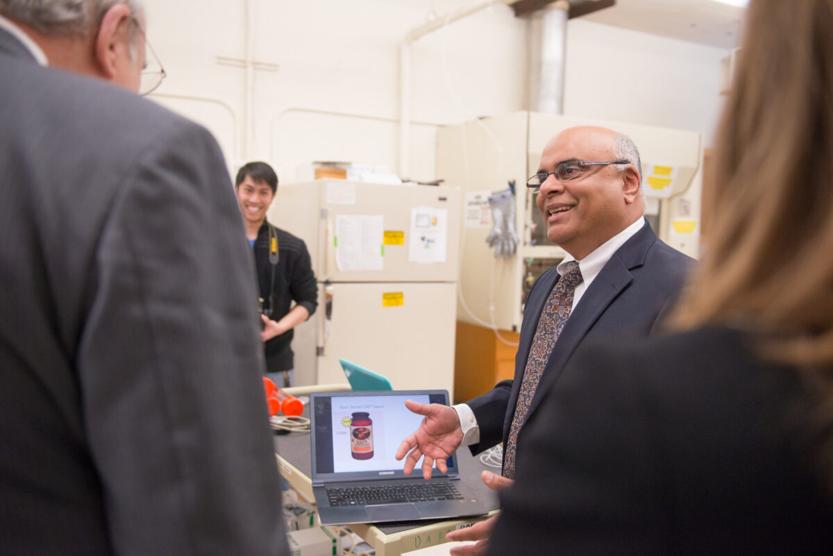 Man smiling while speaking with a few other people in a lab.