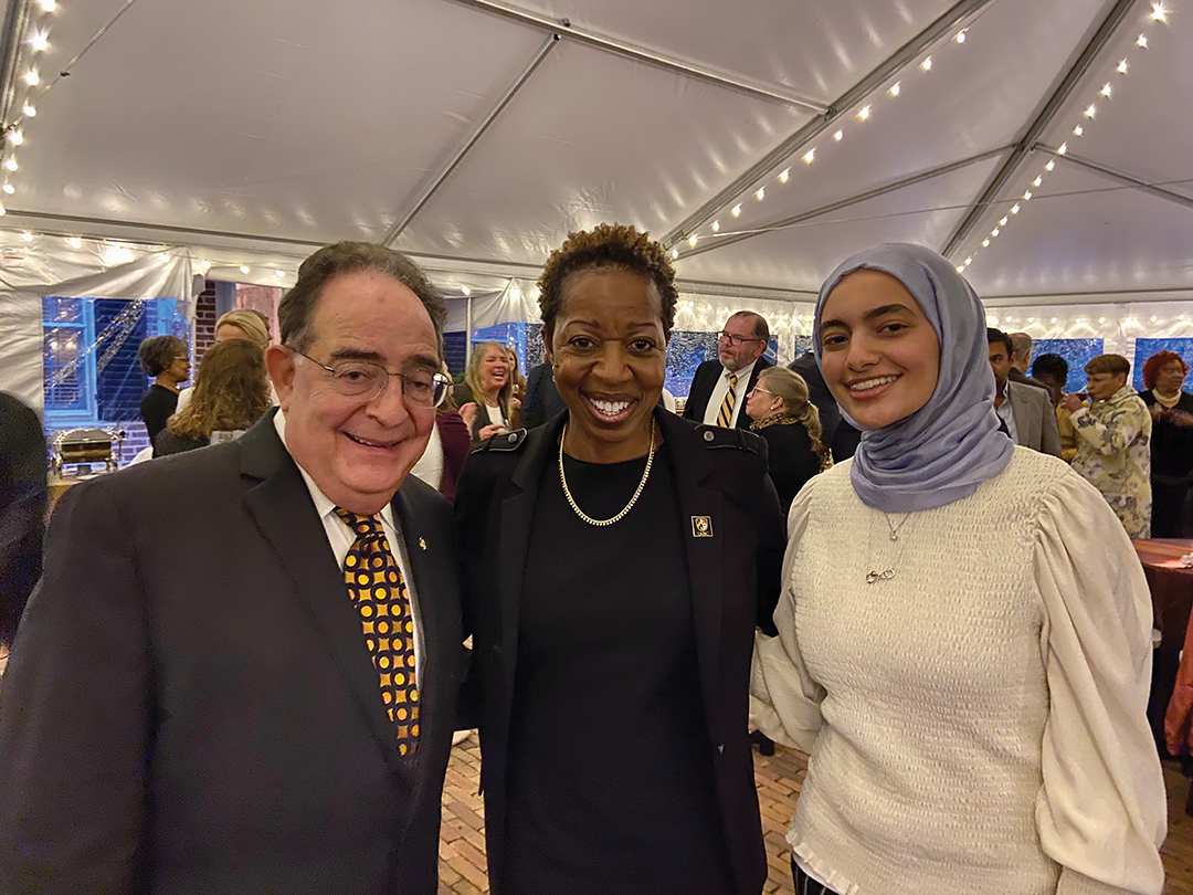 USM Chancellor, President of UMBC, and a student stand in a lit tent at an event.