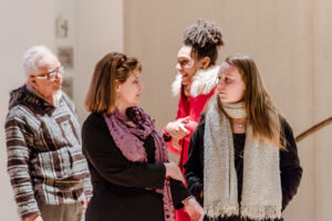 People talk at an art opening at CADVC, Sandra Abbott is center with a purple scarf and shoulder length brown hair