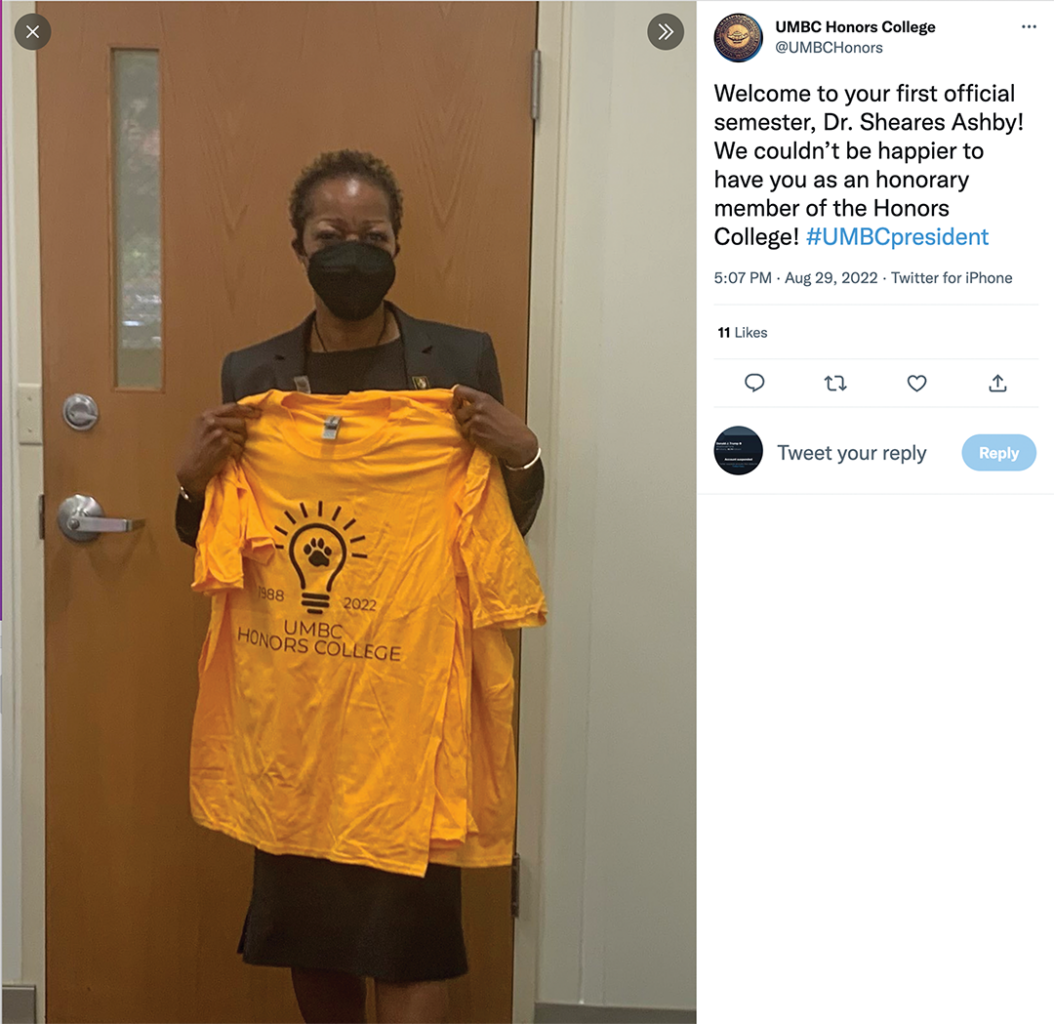Screenshot of an image of the President of UMBC holds up a t-shirt that reads 1988-2022 UMBC Honors College with an image of a lightbulb with a paw print in the center. The tweet reads "welcome to your first official semester, Dr. Sheares Ashby! We couldn't be happier to have you as an honorary member of the Honors College! #UMBCpresident"