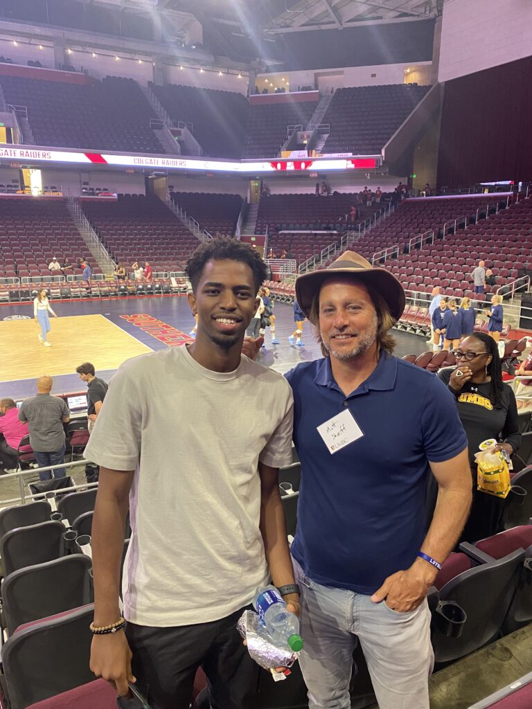 two men stand courtside at a volleyball tournament. They would later become friends and surf together.
    