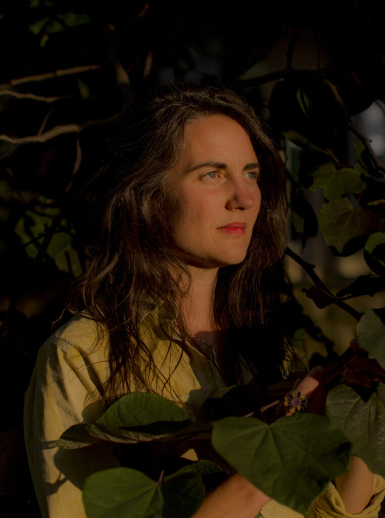 Headshot of Monique Crabb, the artist stands in foliage with deep natural light shining on her face