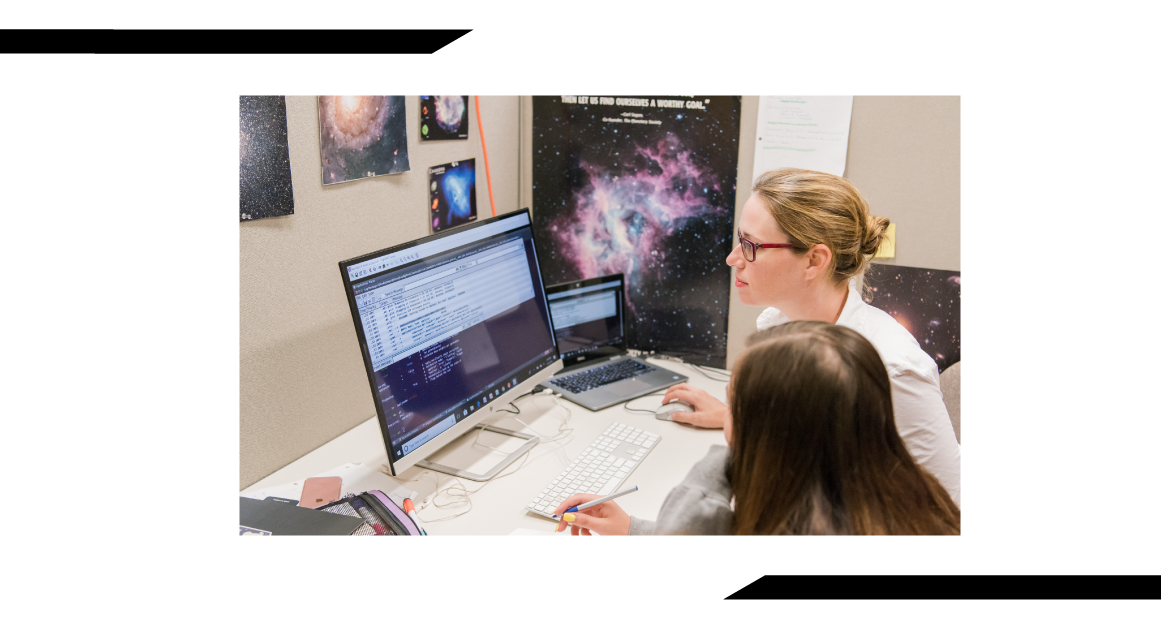 A professor sits at a desk with a student going over data