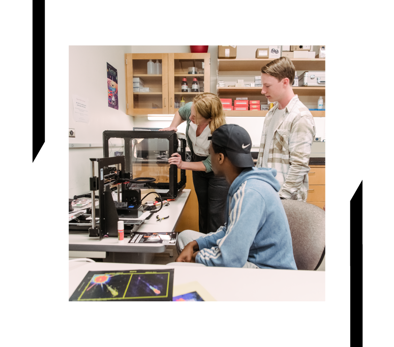 A professor shows a piece of equipment on a desk to two students