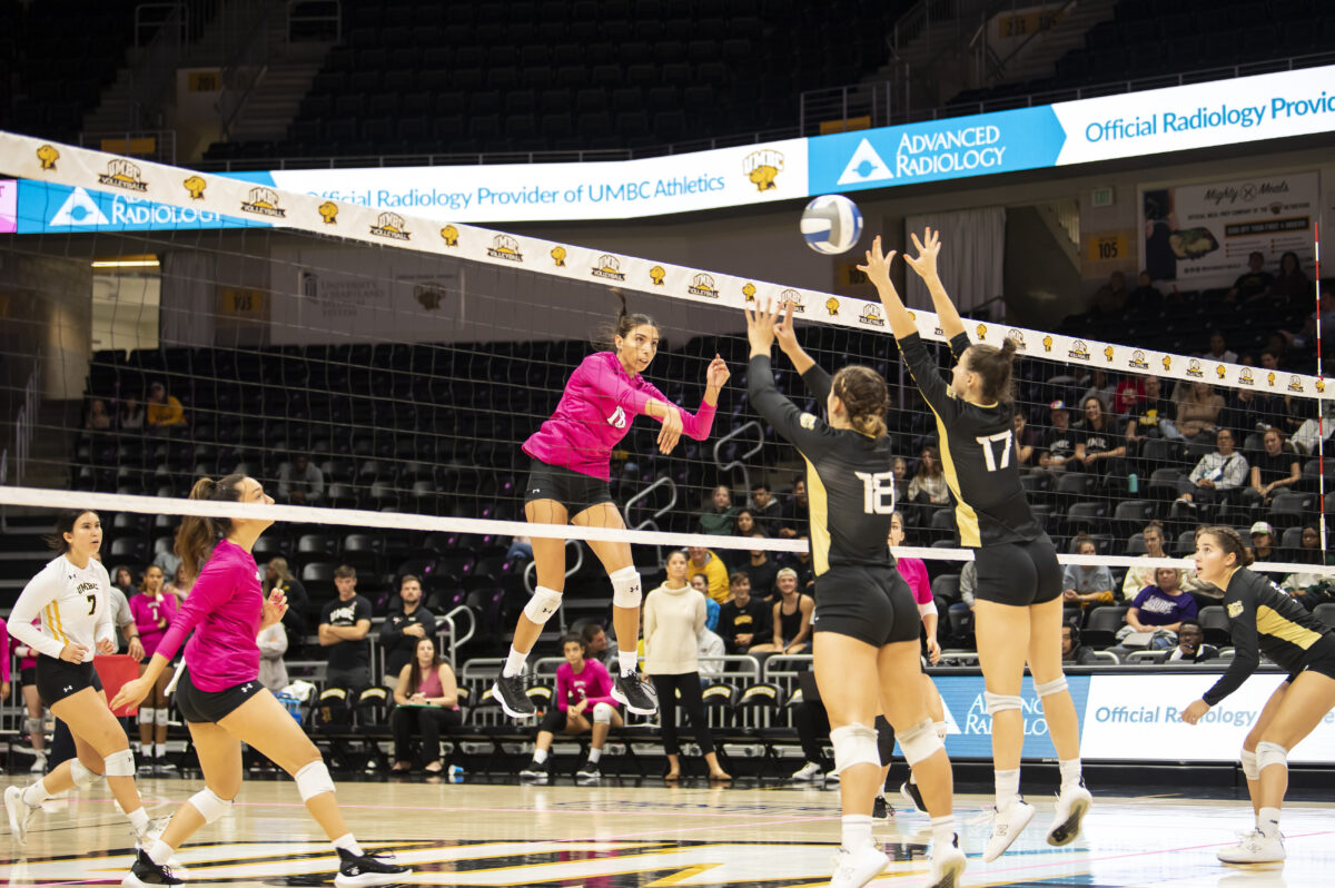 UMBC volleyball team, in pink, hits the ball back over the net to the other team