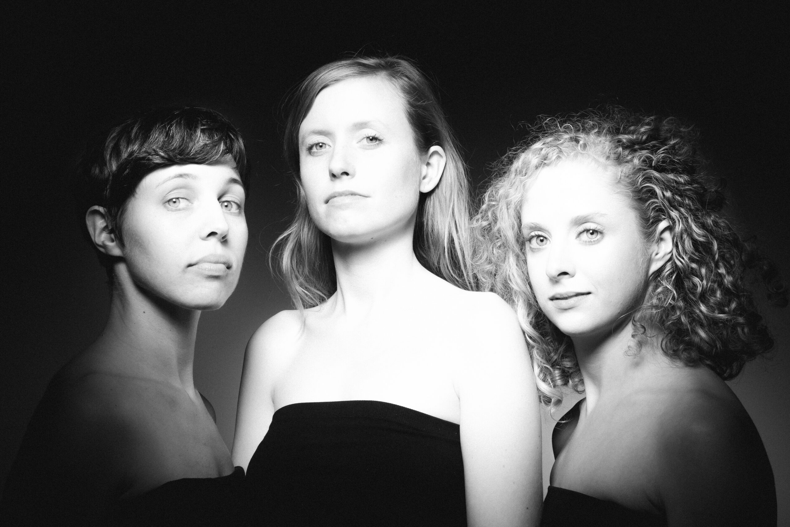 In a black and white photograph, three white women look toward the camera