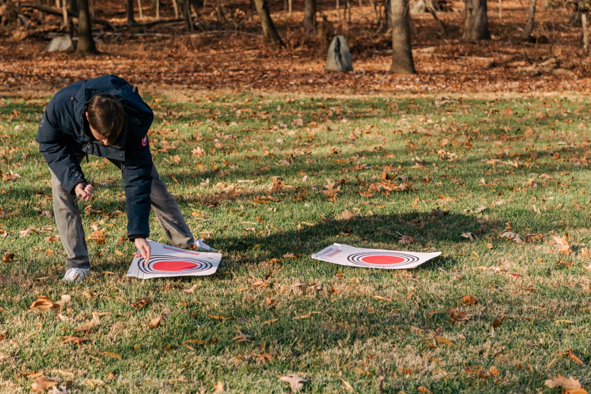 a student places large white pieces of paper with large red concentric circles on them on the grass.