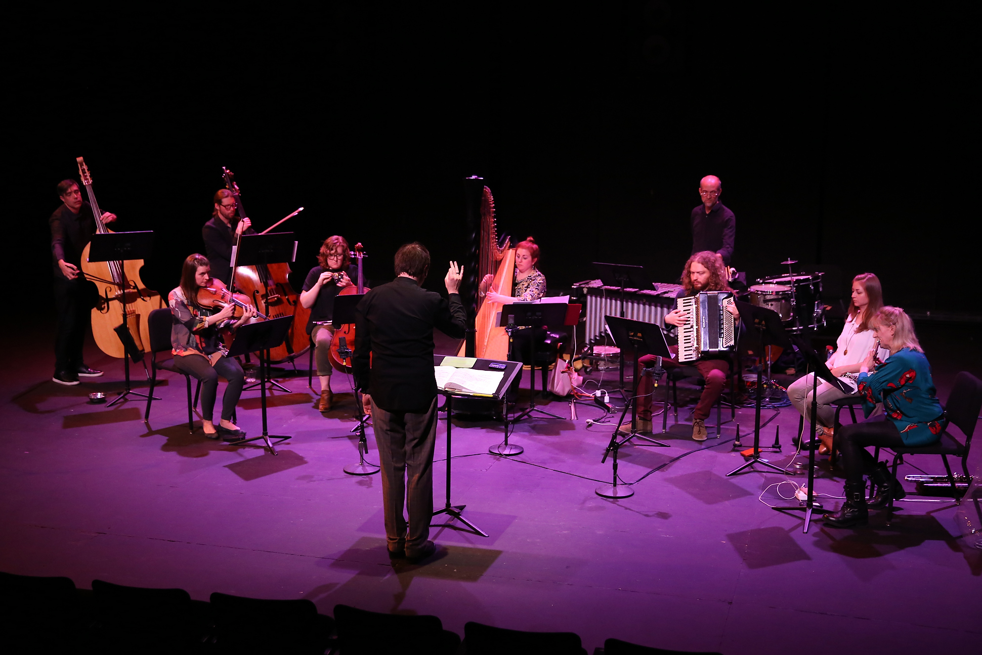 Bathed in violet light, an ensemble of musicians performs on a stage