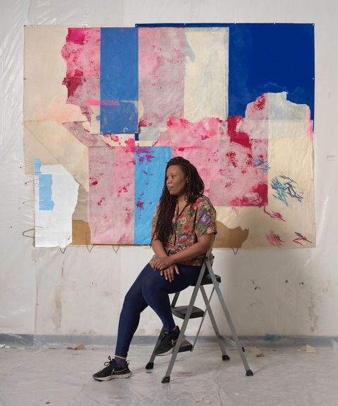 Artist Tomashi Jackson sits on a step stool before an abstract artwork composed of paint and stitchwork on various papers, including unfolded paper bags with handles