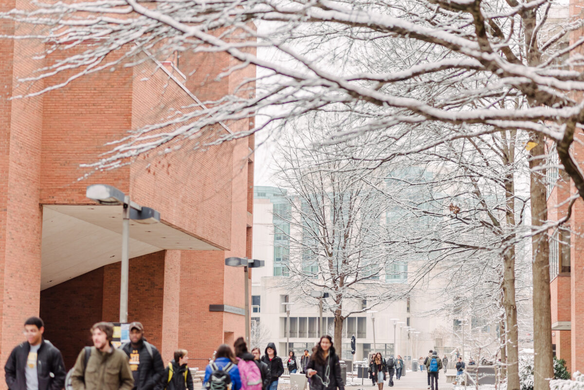 students walking between brick academic buildings; a dusting of snow on the trees