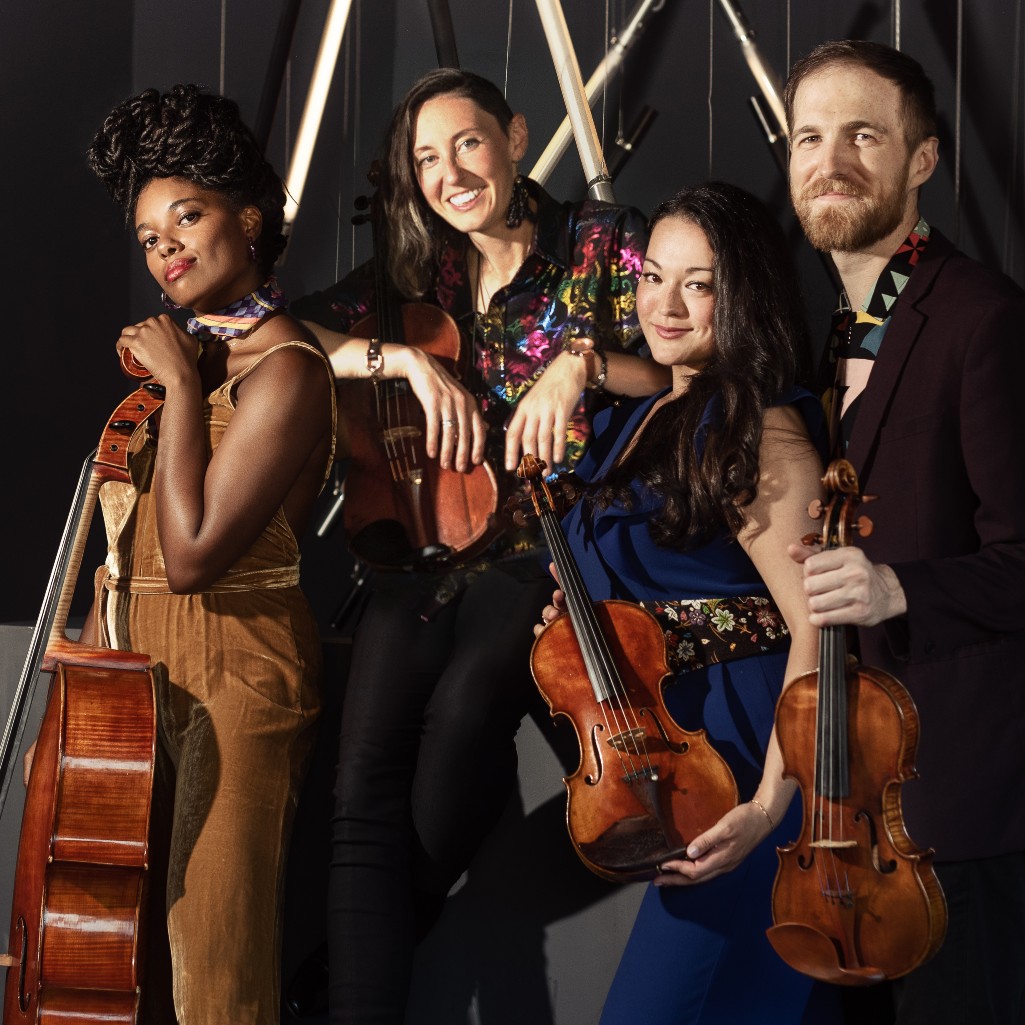 A group of four musicians pose with their string instruments