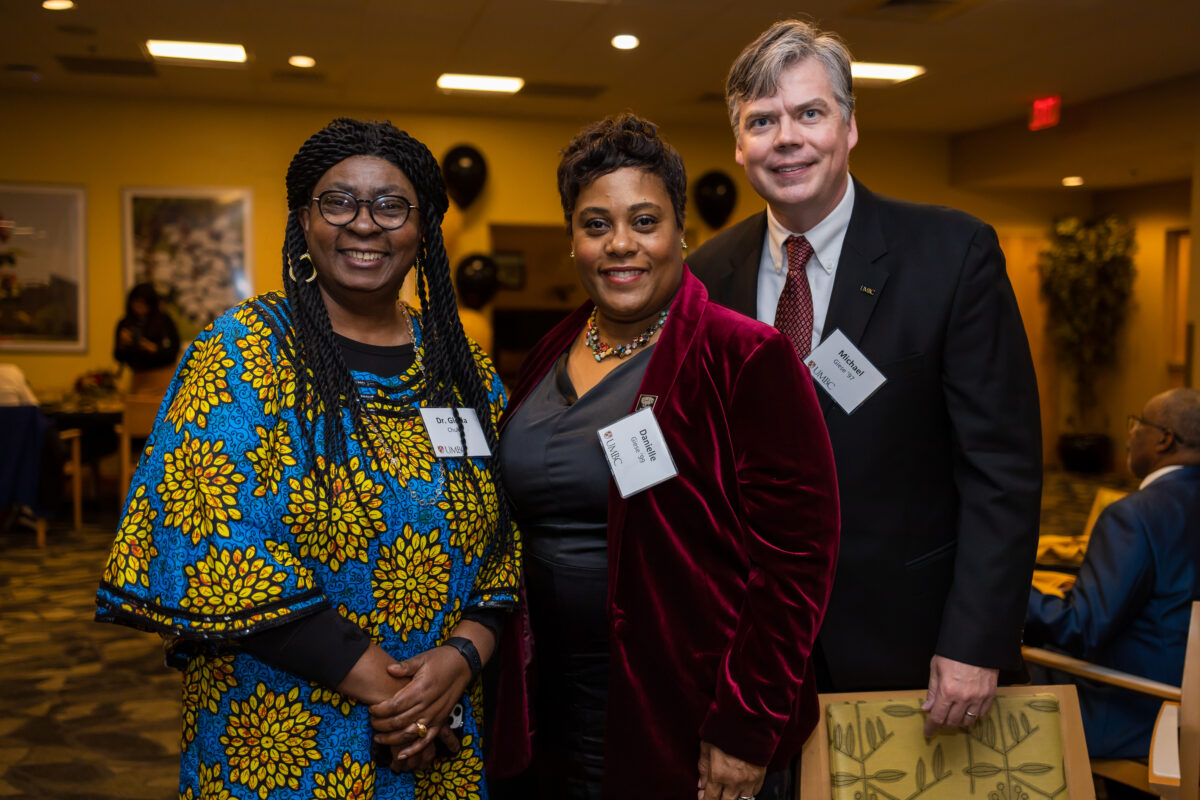 Three adults stand next to each other at an Africana Studies celebration inside a dimly lit room.