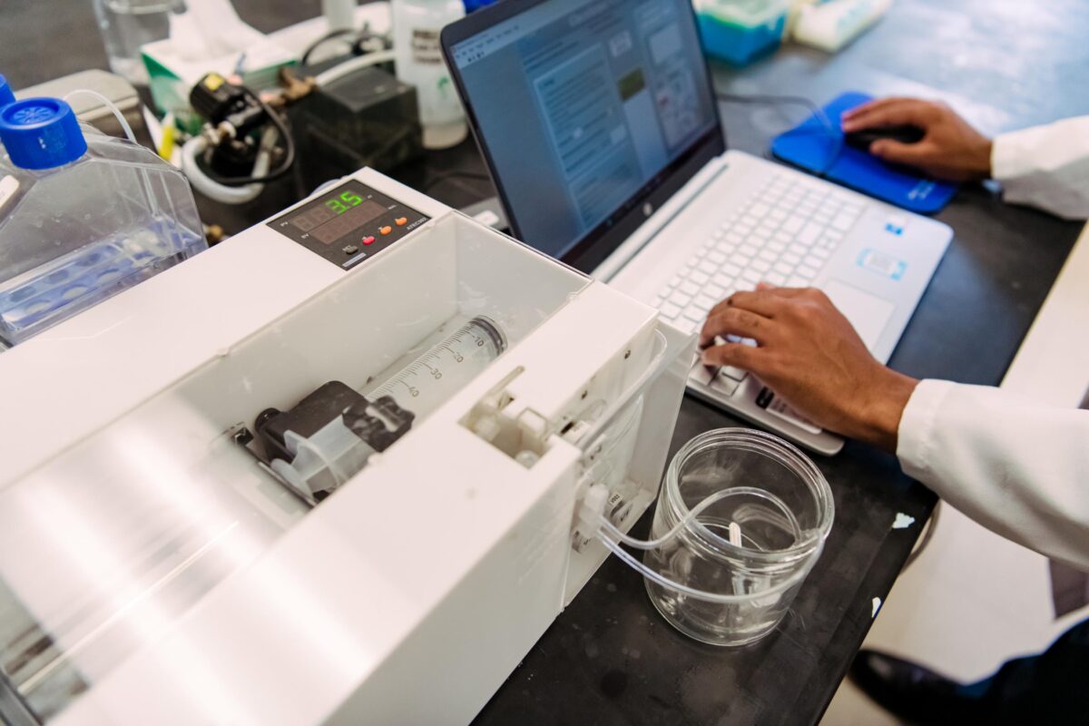 Lab equipment sits on a table. Someone uses a computer near-by.