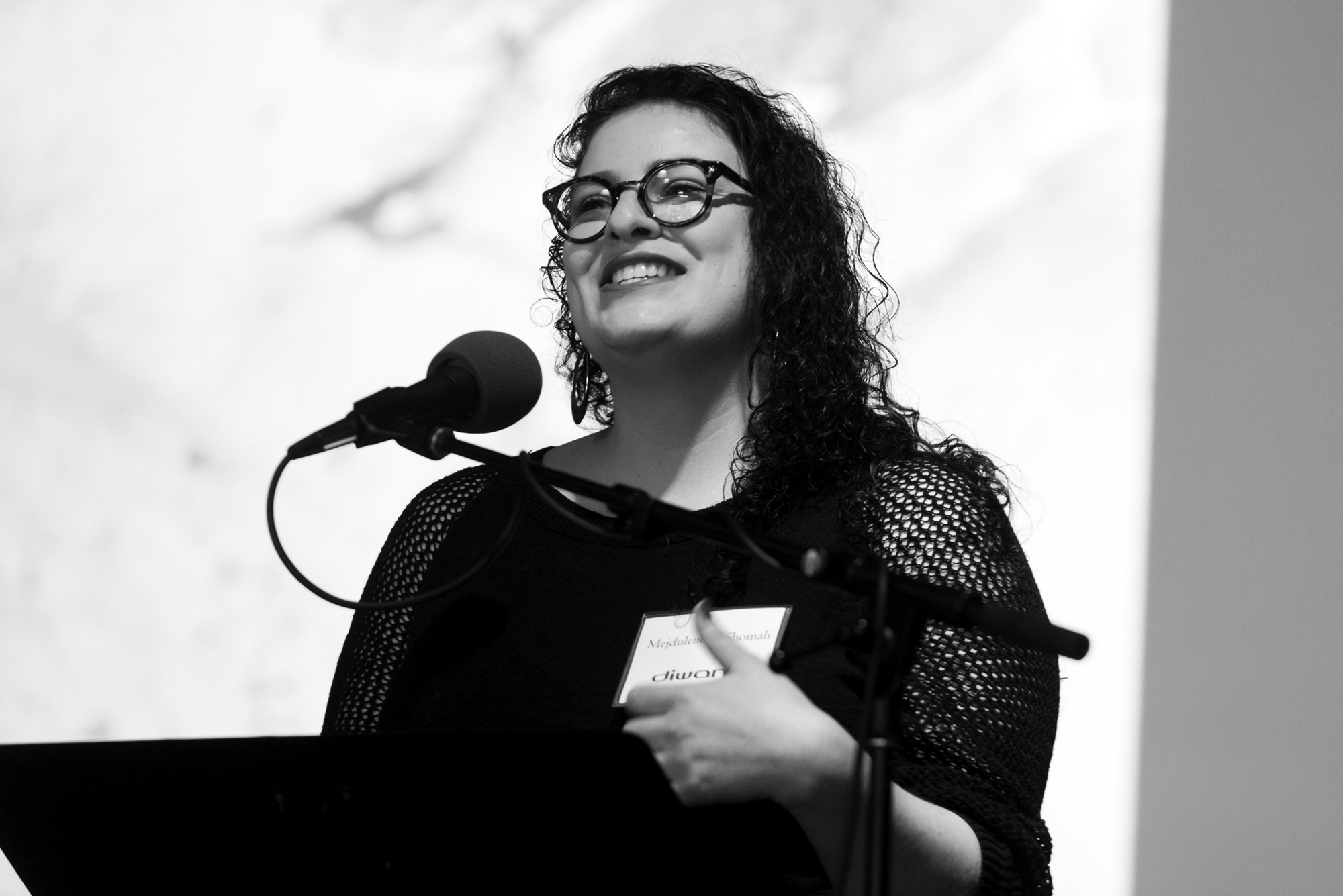 A black and white photo of a Palestinian woman smiling while standing behind a podium.