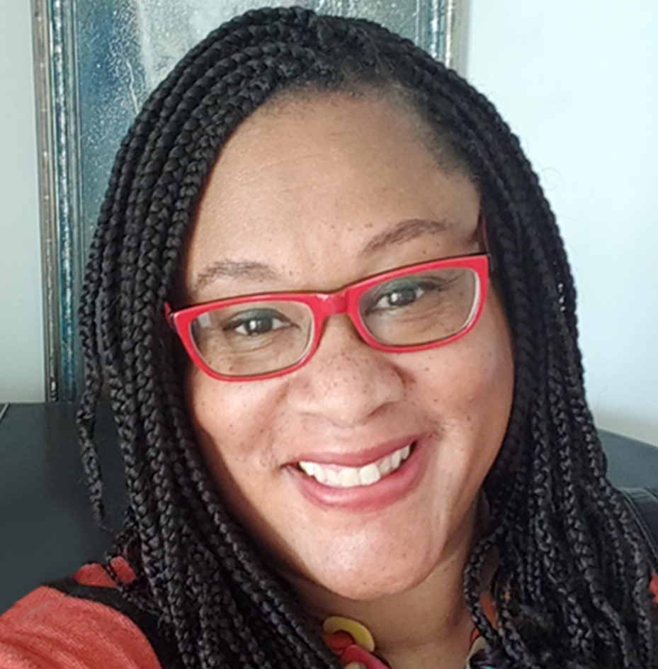A Black woman with red glasses smiles at the camera.