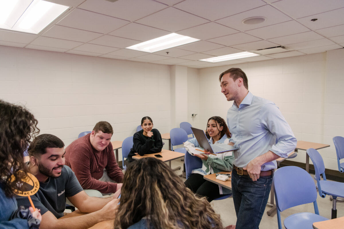 A group of students and a professor engage in conversation in a classroom.