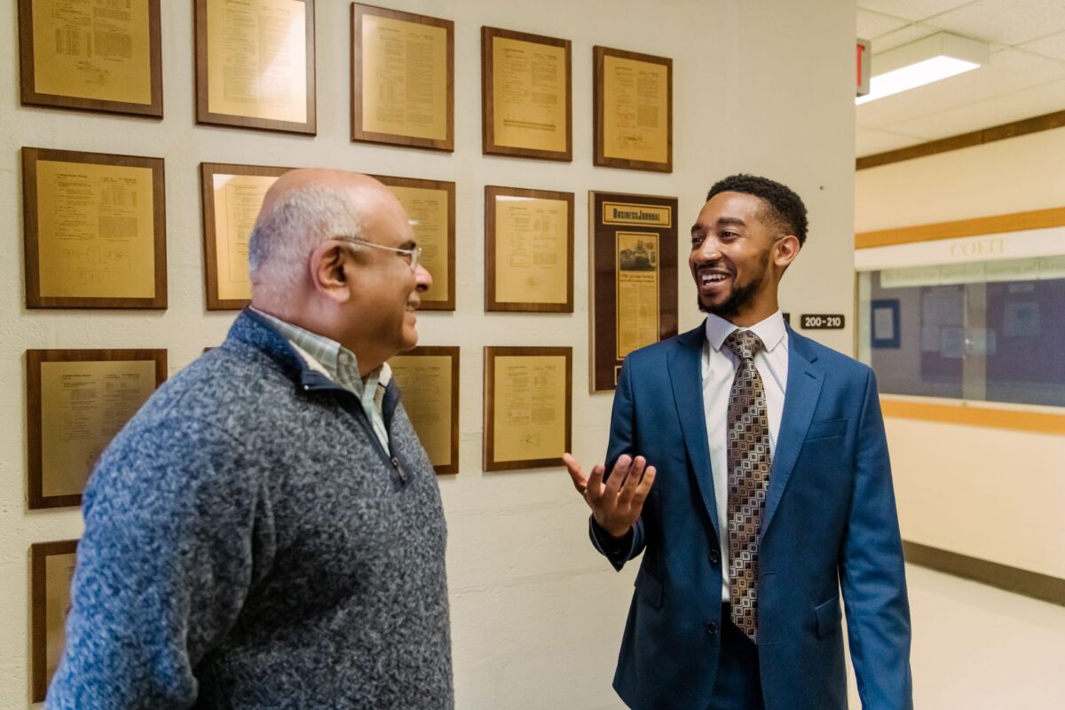 Two people talk in front of a wall of plaques.