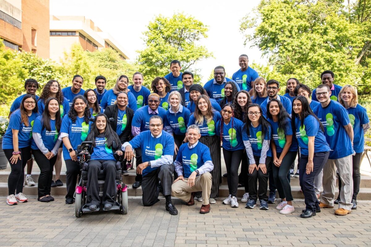 A group of lab members pose together outside, all are wearing the same blue shirt