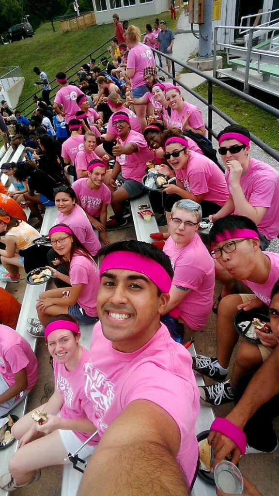 Residential life staff all wearing pink shirts and pink headbands sit on bleachers together