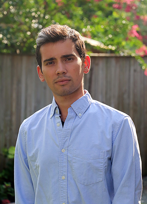 Man wearing a blue dress shirt, standing outside, with a contemplative facial expression