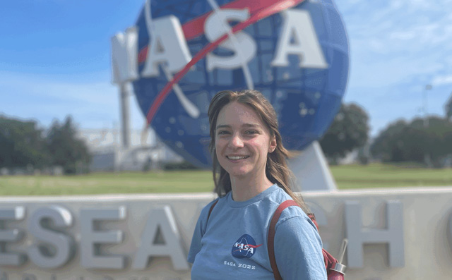 A young white woman stands in front of a NASA sign