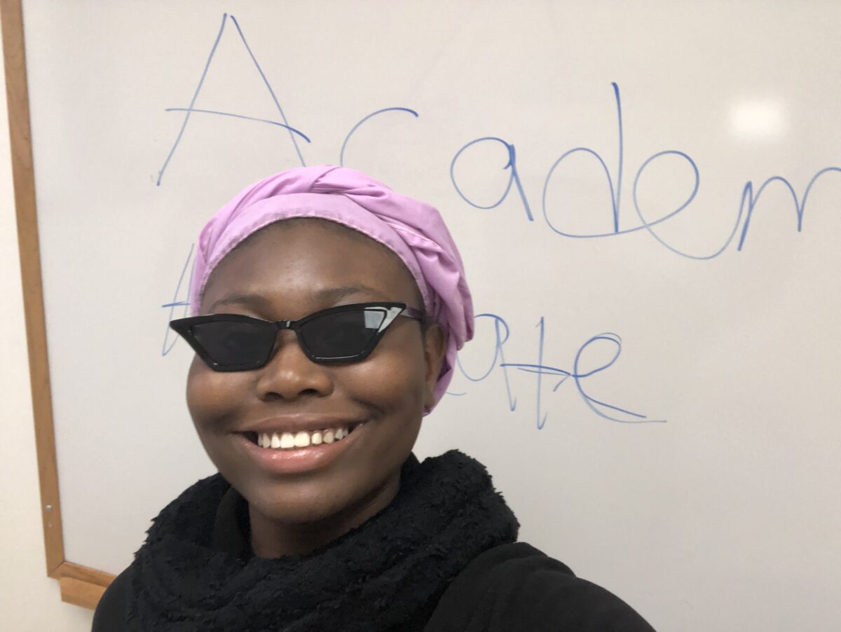 A woman wearing sunglasses smiles at the camera. She is an academic peer advocate.