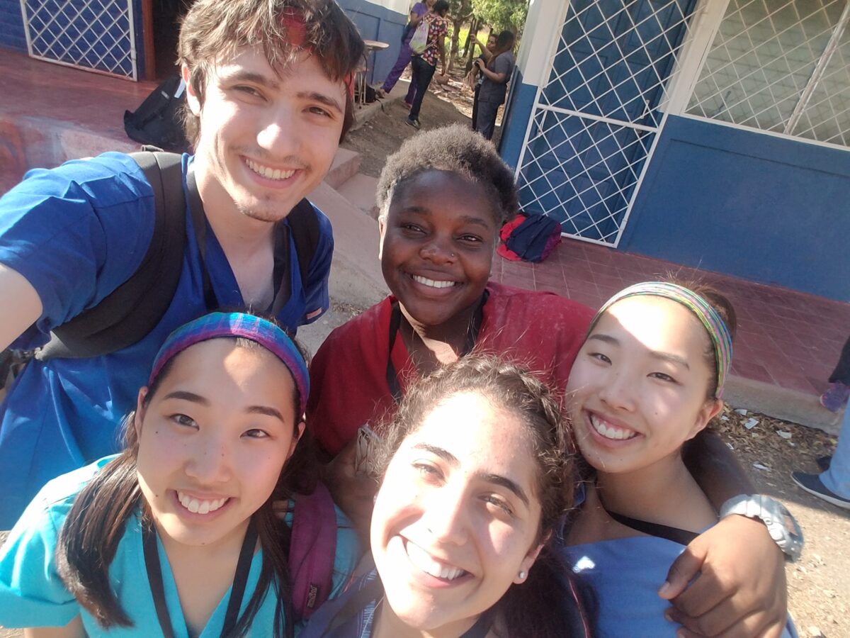 A group of Global Brigades volunteers huddle together on a sunny day in front of a blue and white concrete building. exploring new science opportunities
    