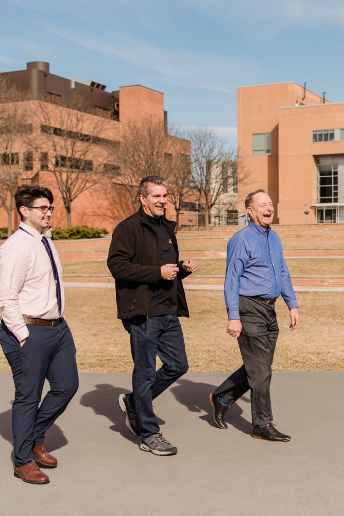 Three man walk across a campus quad, laughing together