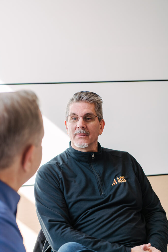 A man in a black zip up talks animatedly with someone off camera