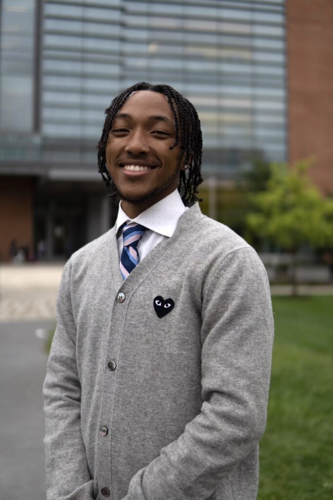 Headshot of a young man in a buttoned up sweater and a tie with a white shirt