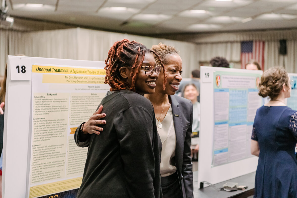 Two women smiling in posing for a picture in front of a research poster board. 