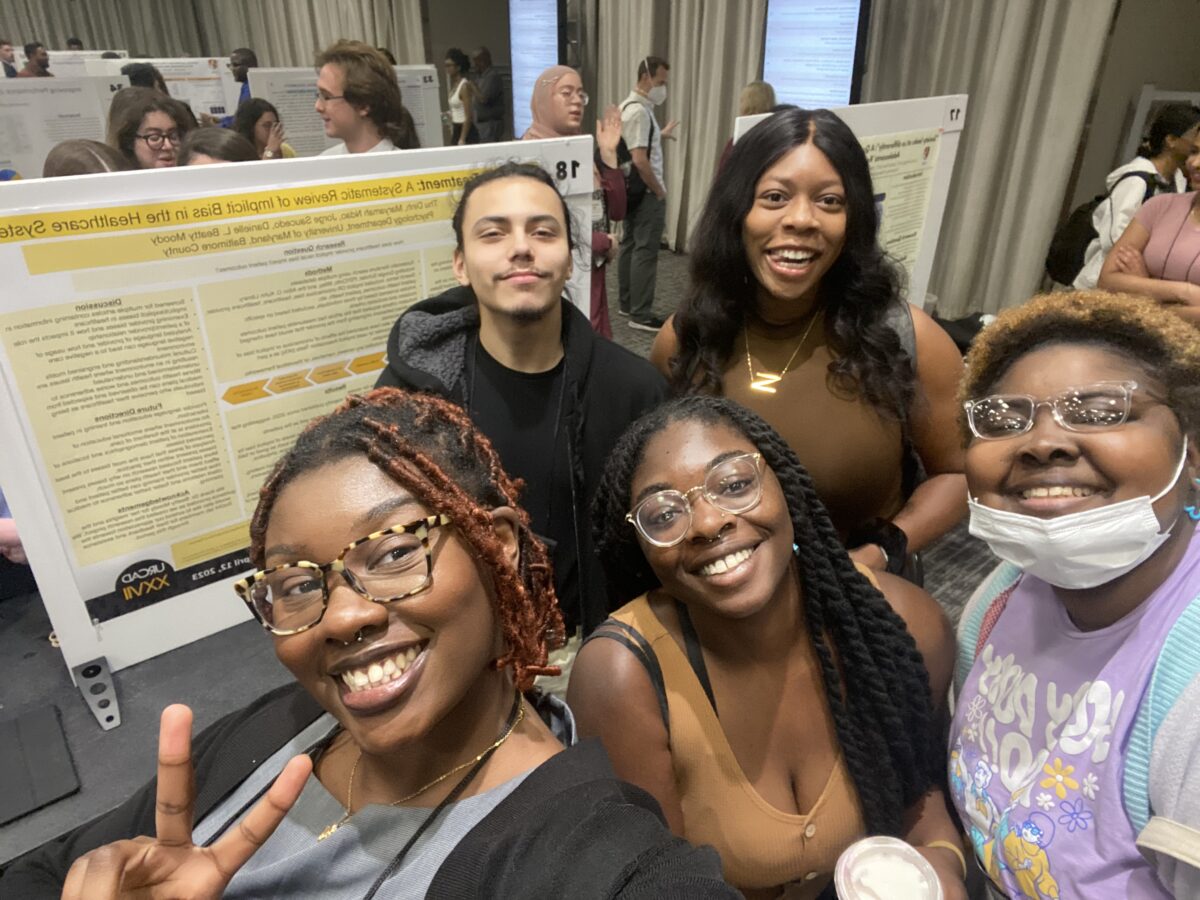 Five students smiling and posing for photo in front of their research poster board at URCAD 2023.