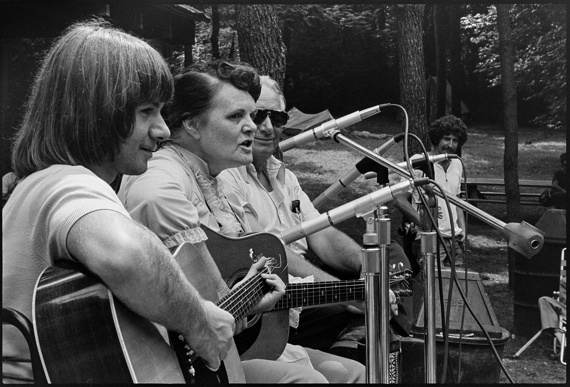 In an old black-and-white photograph, a trio of musicians sing and play guitars