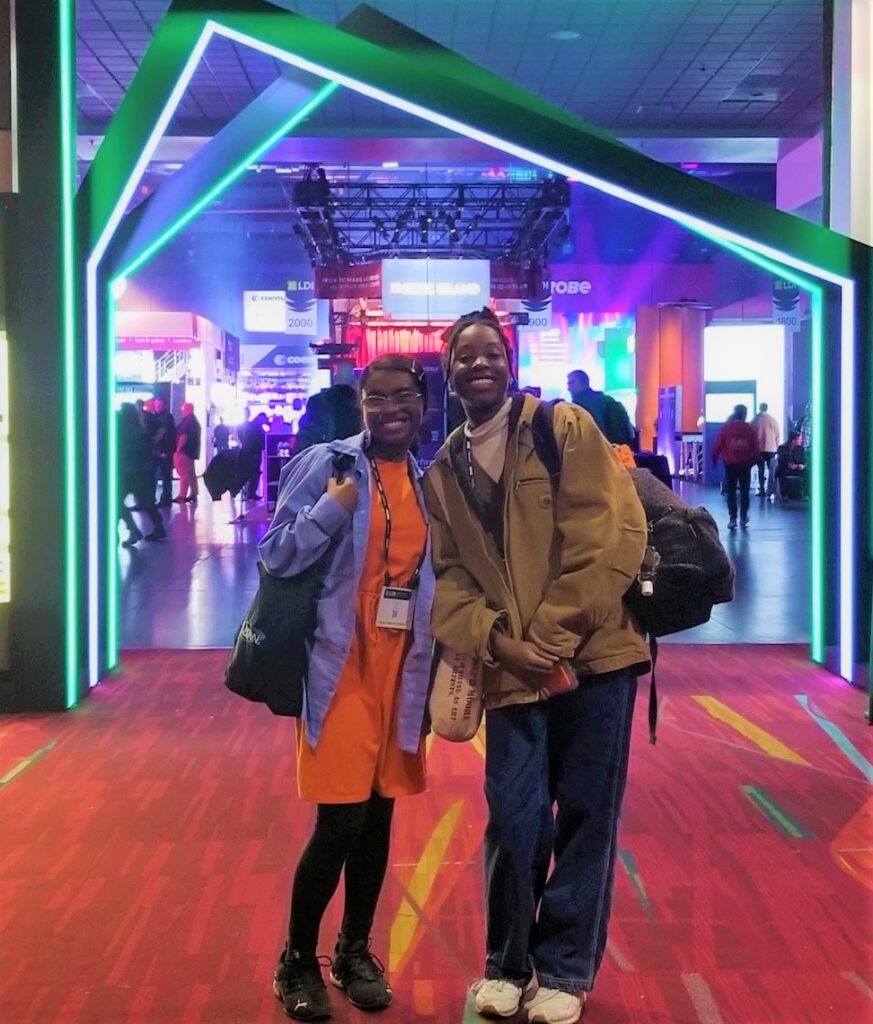 Two students smiling in front of a display at a conference and trade show