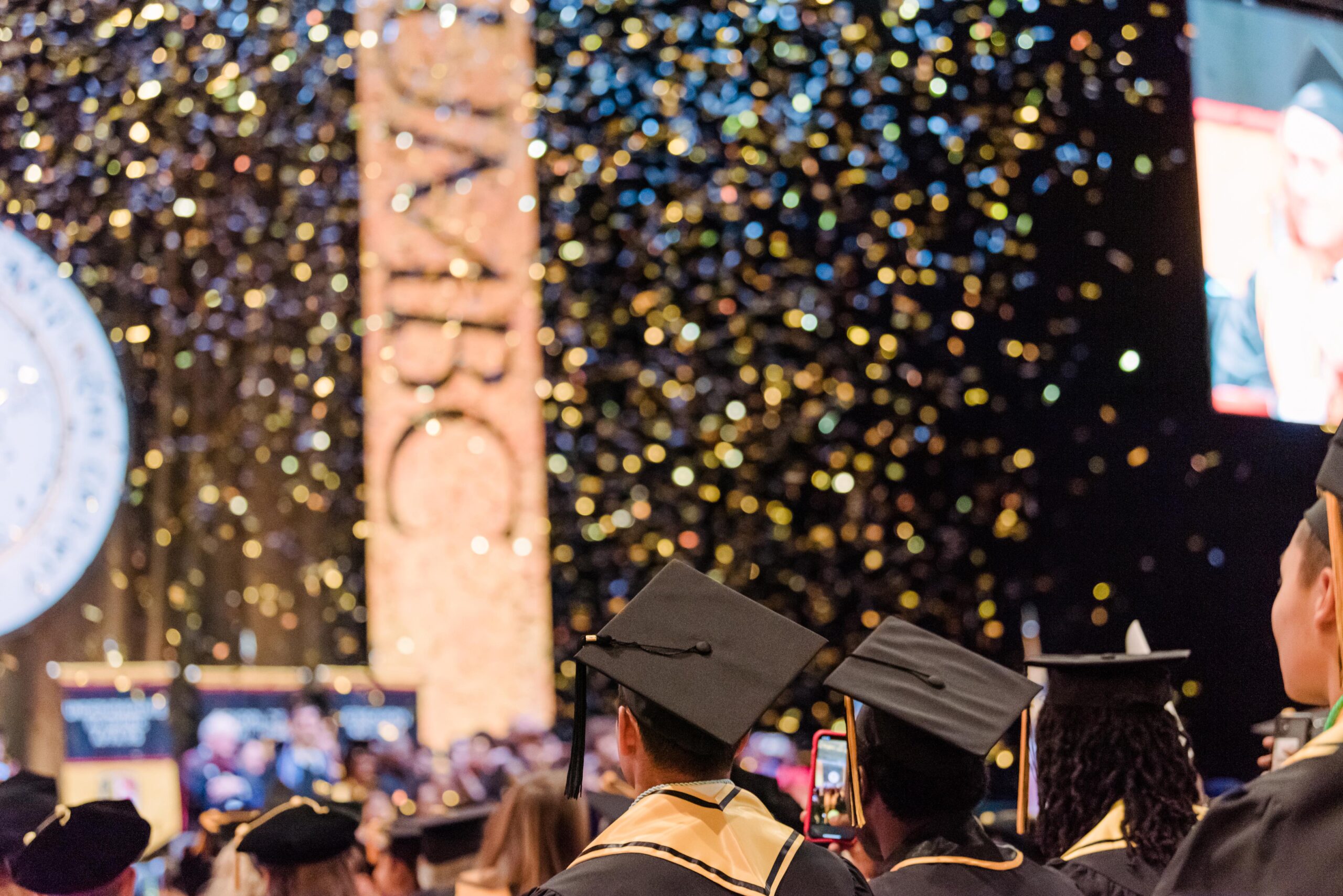 Graduates stand under gold confetti during commencement celebrations.