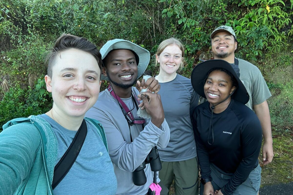 Group of five people in fieldwork clothing, one holding a small bird. Tropical forest in the background.