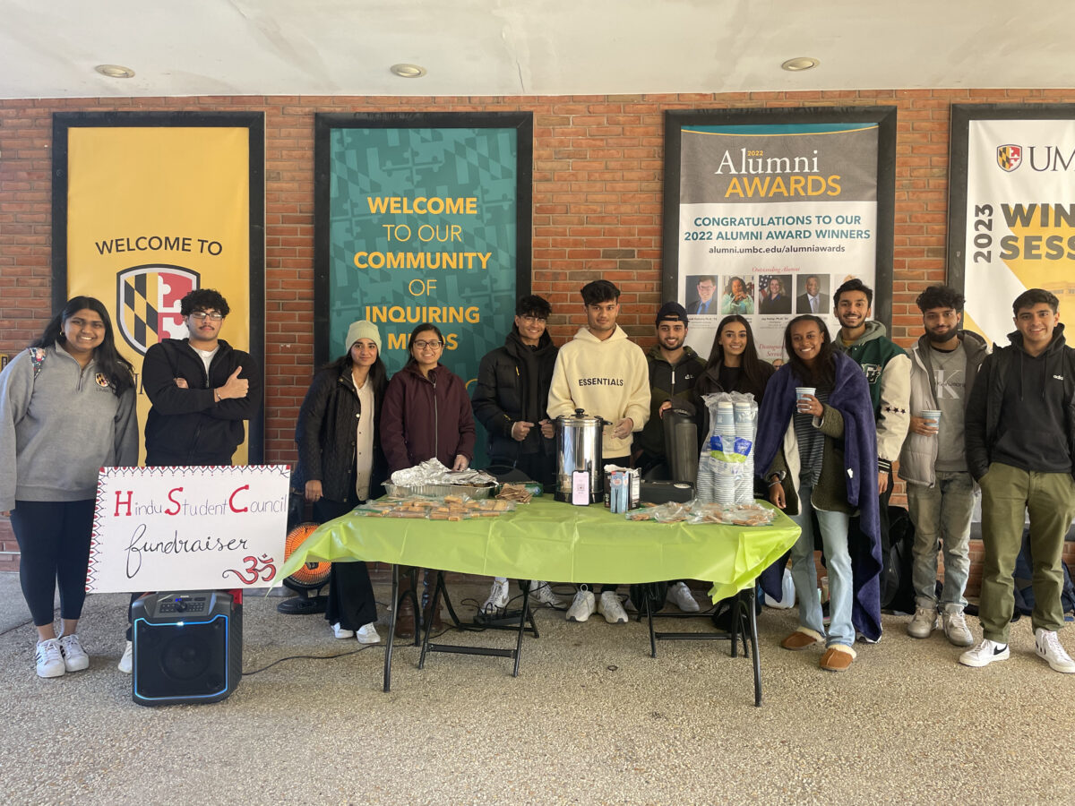 Students stand at a snack table with a sign reading "Hindu Student Council fundraiser" and UMBC banners in the background.