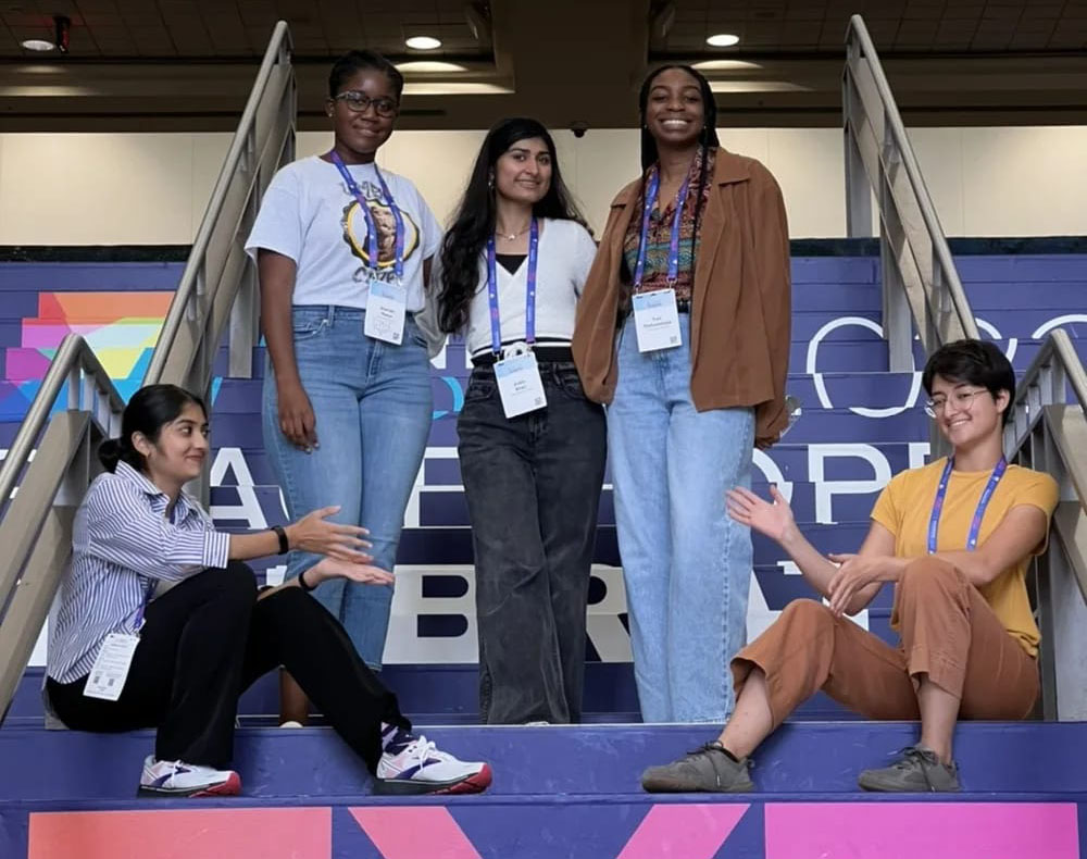 5 people pose for camera, 3 stand in the middle, 2 are seated on either side.