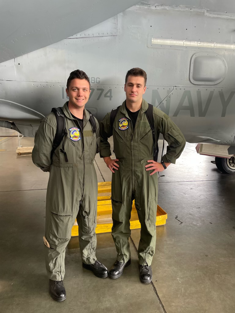 Two men in uniform stand in front of a Navy plane.