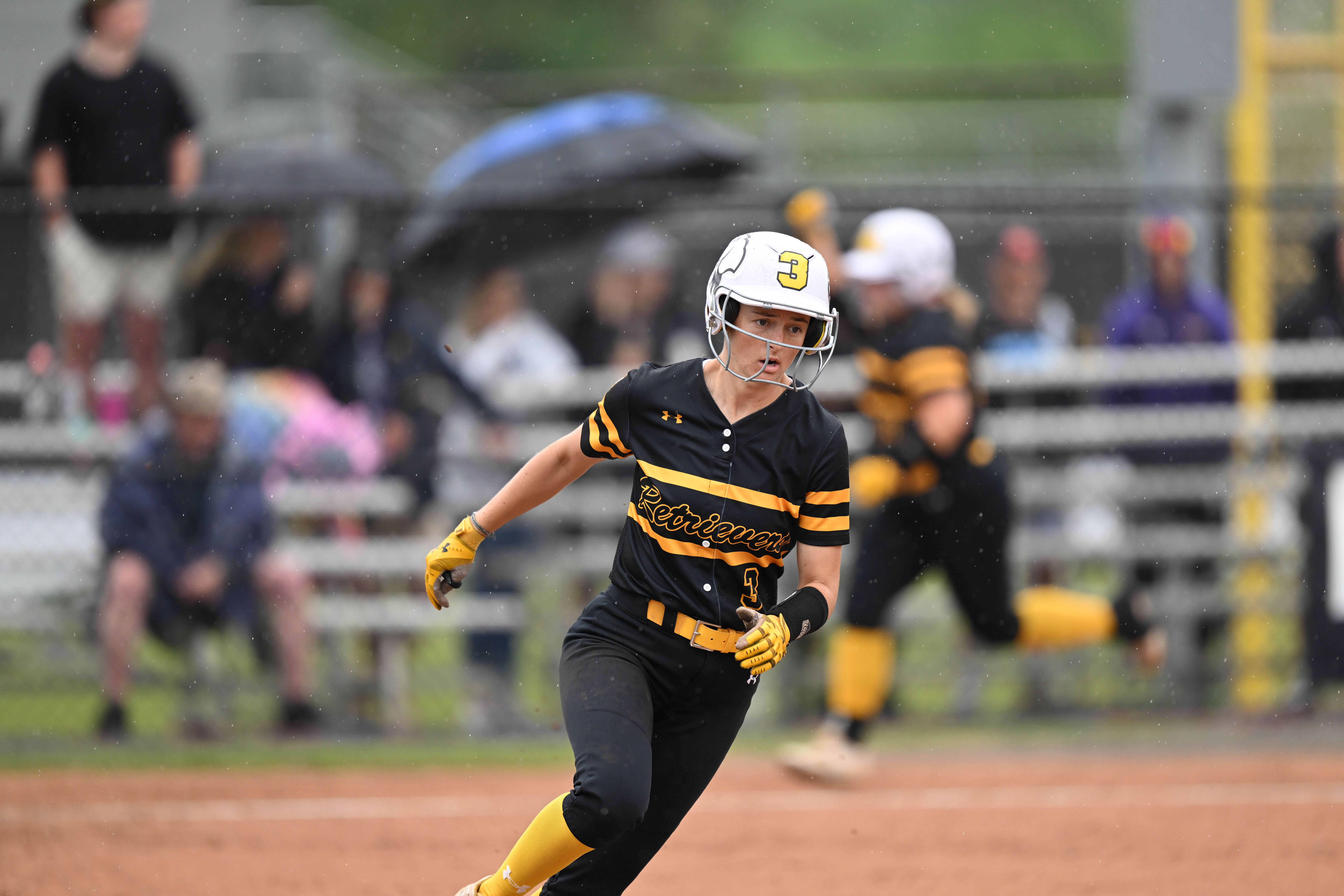 A softball player with a helmet on and a black and gold UMBC uniform runs the bases