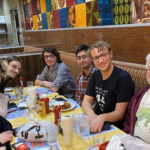 A group of people are seated around a dining table. They smile at the camera.