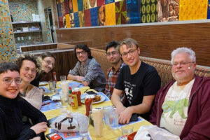 A group of people are seated around a dining table. They smile at the camera.