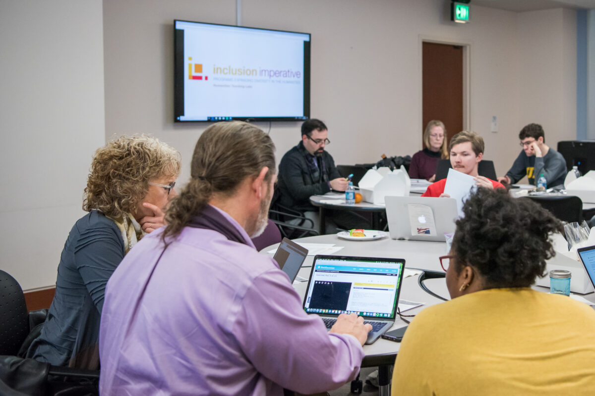 Groups of people sit at round tables working on their laptops at a UMBC Dresher Center for the Humanities Teaching Lab.