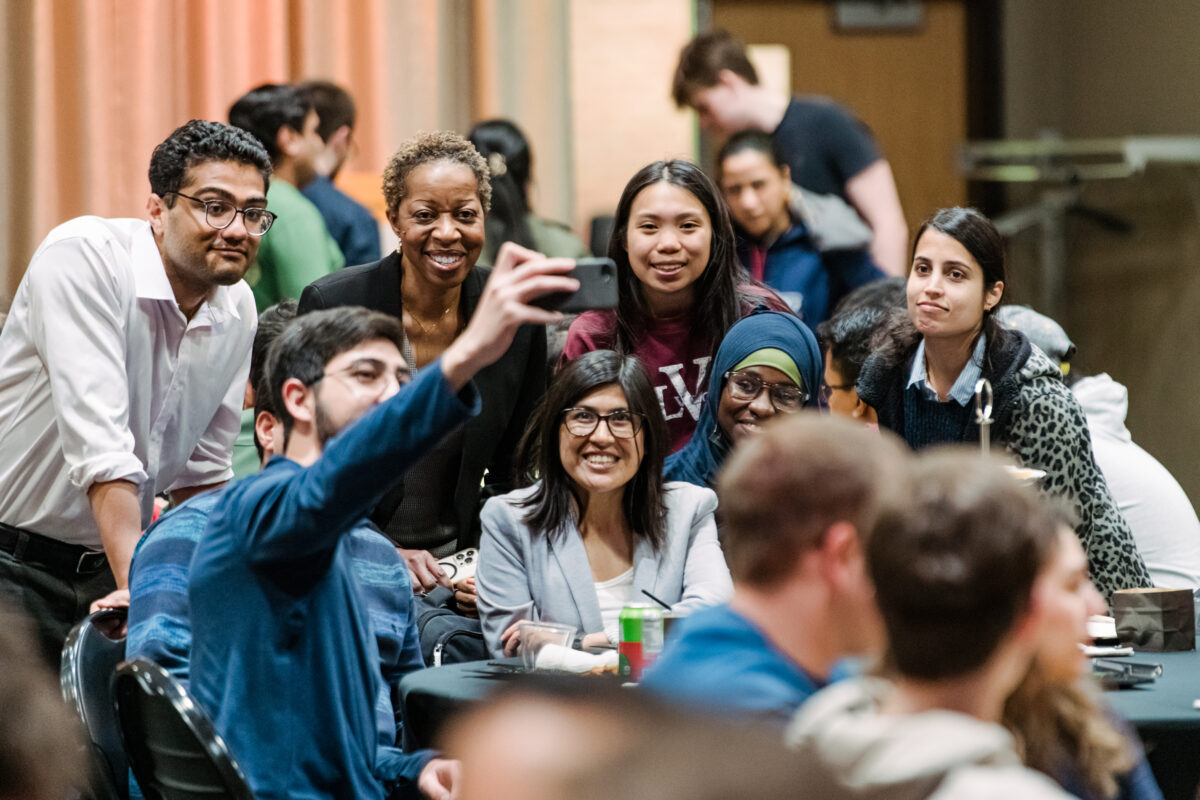 graduate students gather around a table to take a selfie with president sheares ashby